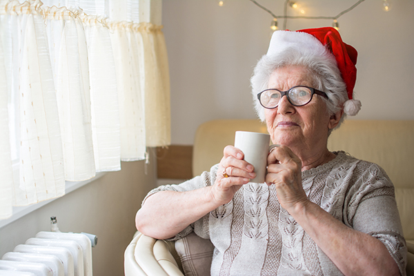 Senior woman with red Santa's hat holding hot tea and looking through window. Xmas, home, age, alone, senior concept.