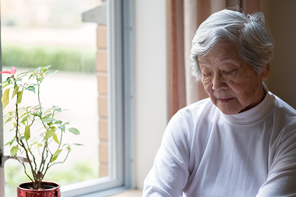 Lonely, Senior Woman Sitting by Window with Eyes Closed