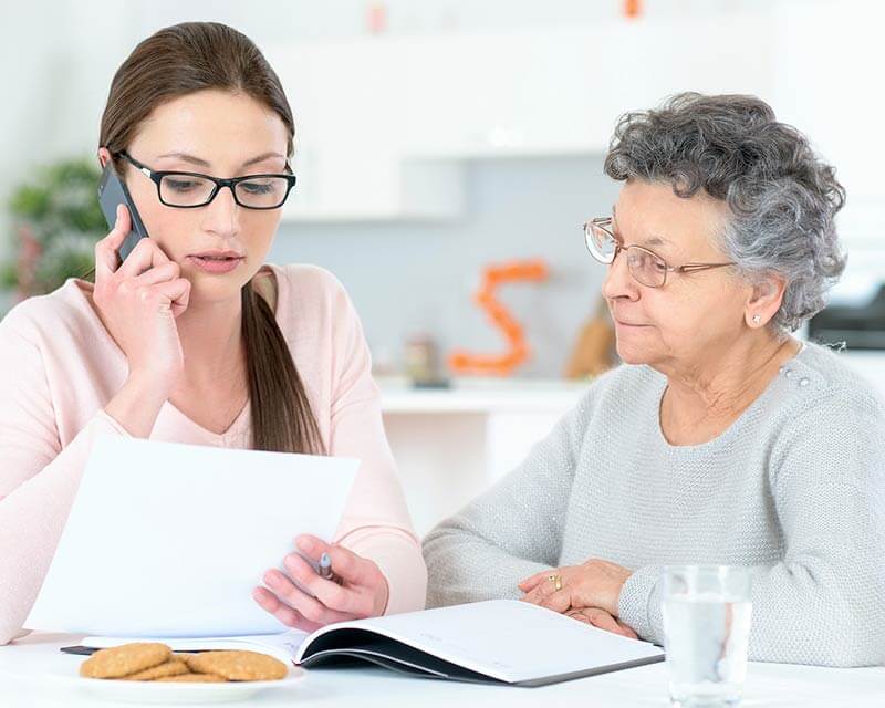 Daughter talking on phone with agency with mother sitting at table