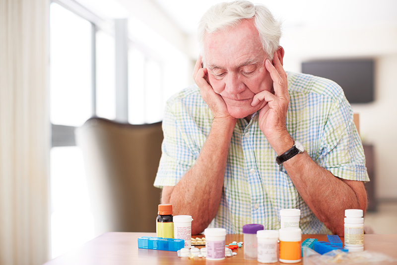 Senior man sitting and looking at his medication despondantly