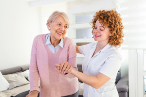Smiling nurse helping senior lady to walk around the nursing home. Portrait of happy female caregiver and senior woman walking together at home. Professional caregiver taking care of elderly woman