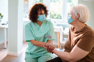 masked caregivering comforting senior masked woman