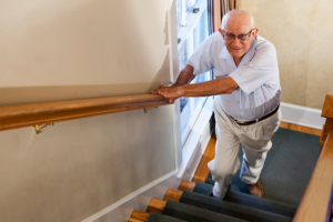 senior man holding onto railing while walking up stairs