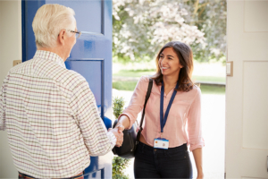 An older man smiles at and shakes the hand of a new caregiver, a first step to helping make a caregiver feel welcome.