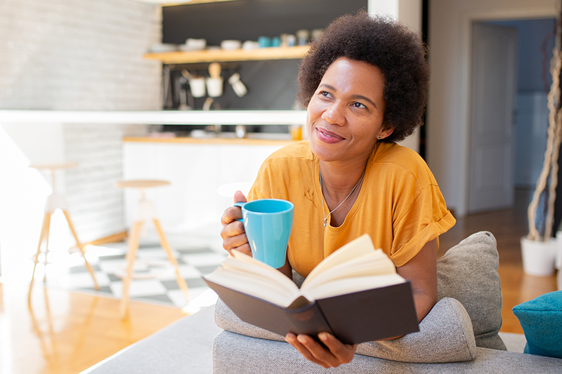 A woman enjoys a cup of tea while reading a book because she has found a way to prioritize privacy as a caregiver.