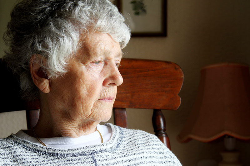 An elderly woman sits in a chair staring into the distance as she experiences boredom’s impact on dementia.