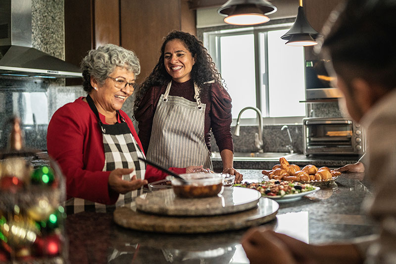 A family smiles while cooking together in the kitchen during the holidays after implementing some stress-relief tips for caregivers.