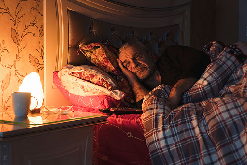 An older man lies awake in bed at night, a common occurrence for many who need to improve senior sleep quality.
