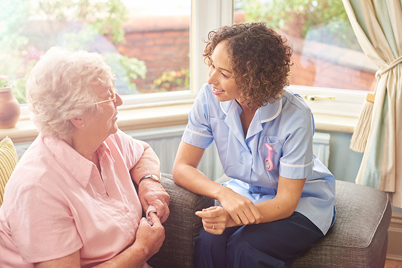 An older woman and her respite care provider enjoy a friendly conversation at home.