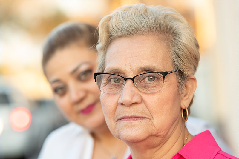 A woman stands behind her elderly mother out of focus, a symbol of how many people don’t focus on what family caregivers really need.
