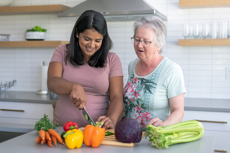 A woman watches her chronic care management provider in Huntington Beach chop vegetables in the kitchen.