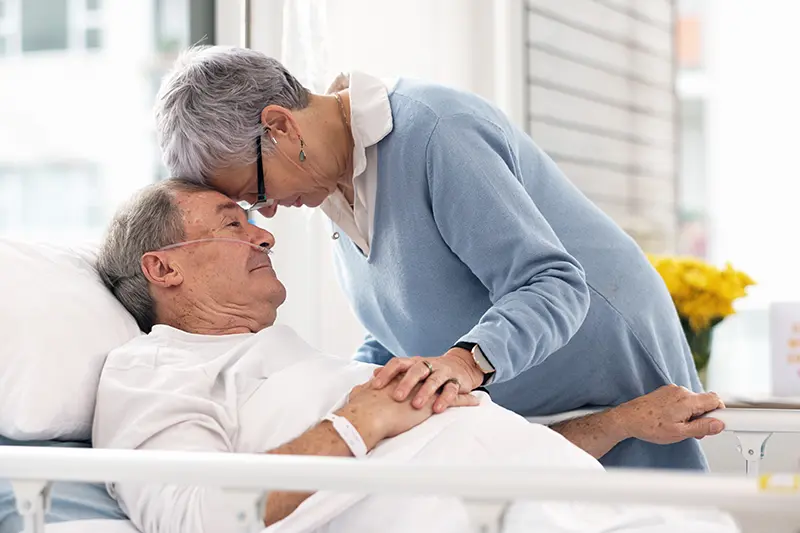 A caregiver offers reassurance to her elderly husband during a hospital stay with dementia.
