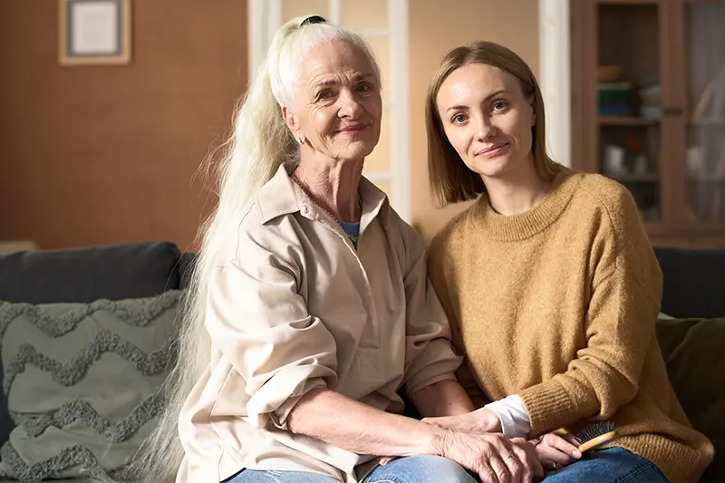 A woman living with Alzheimer’s sits on a couch with her younger family member.